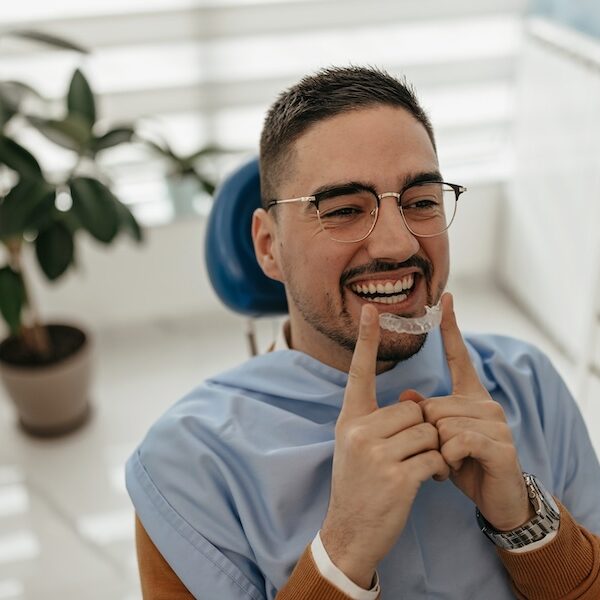 man in dental chair holding Invisalign clear aligner for orthodontics