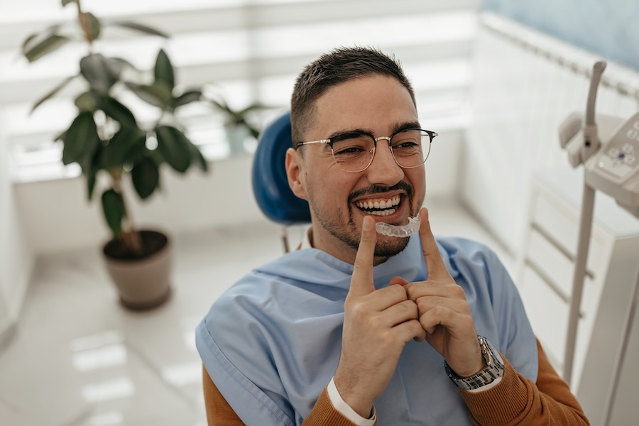 man in dental chair holding Invisalign clear aligner for orthodontics